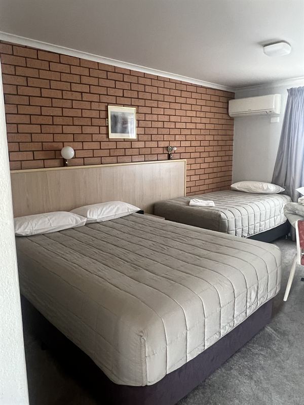 A family room with a queen bed and a single bed against a brick feature wall
