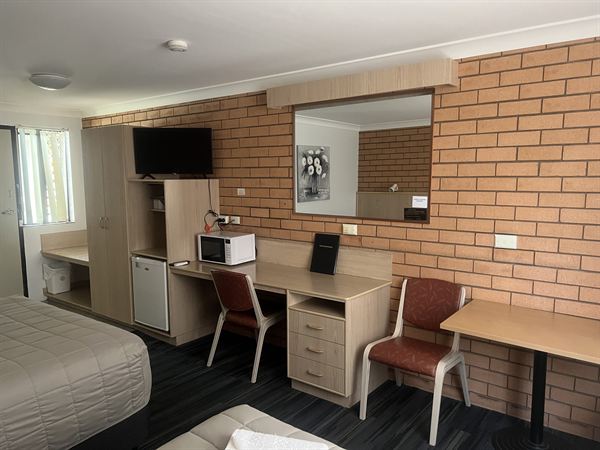 A studio room with a work desk, mirror, microwave, bar fridge and wall-mounted television